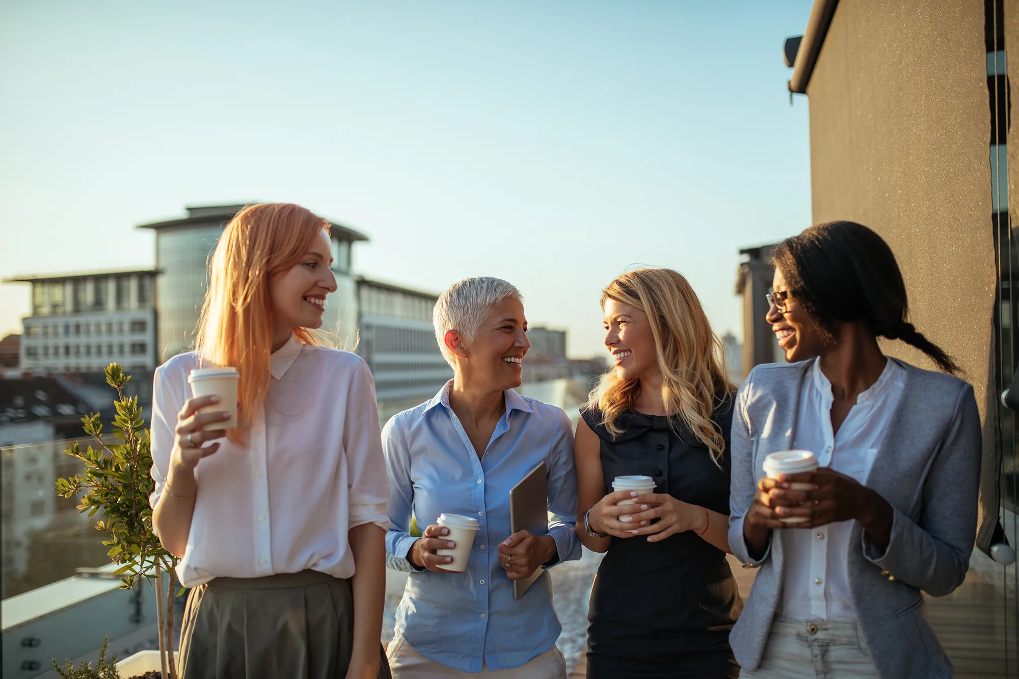 Groupe de femmes &eacute;changeant et partageant un moment convivial en ext&eacute;rieur autour d&rsquo;un caf&eacute;, dans un contexte professionnel et collaboratif en fin de journ&eacute;e